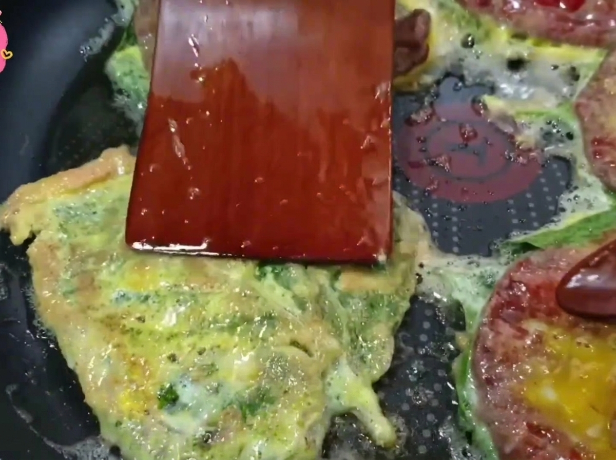 Una espátula de madera dando la vuelta a una tortita de ternera dorada en una sartén caliente.