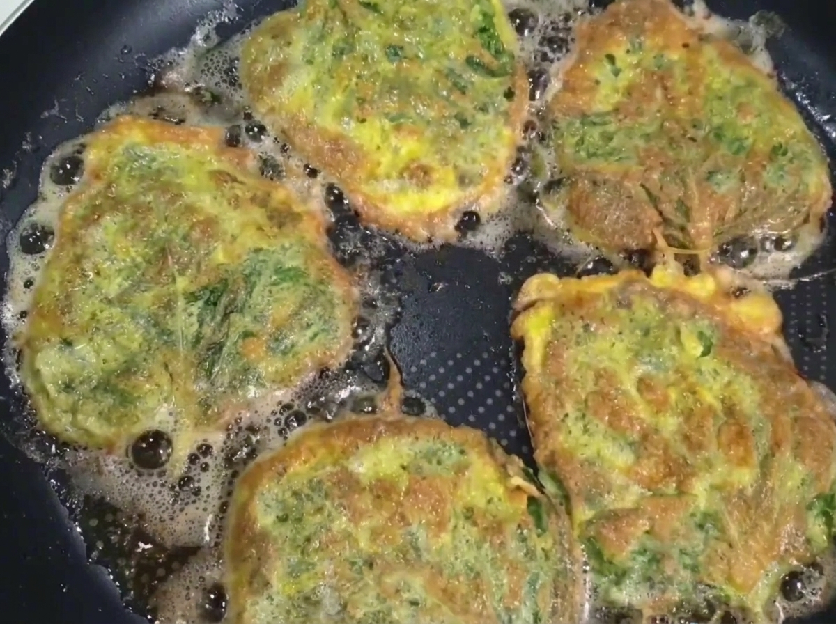 Una tortita de carne y perilla recién hecha siendo levantada de la sartén con una espátula y palillos.