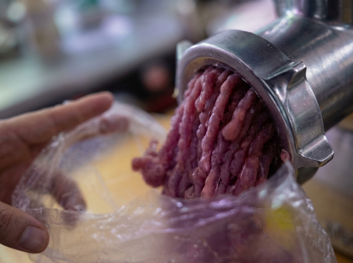 Carne picada saliendo de una picadora de carne mecánica hacia una bolsa de plástico.