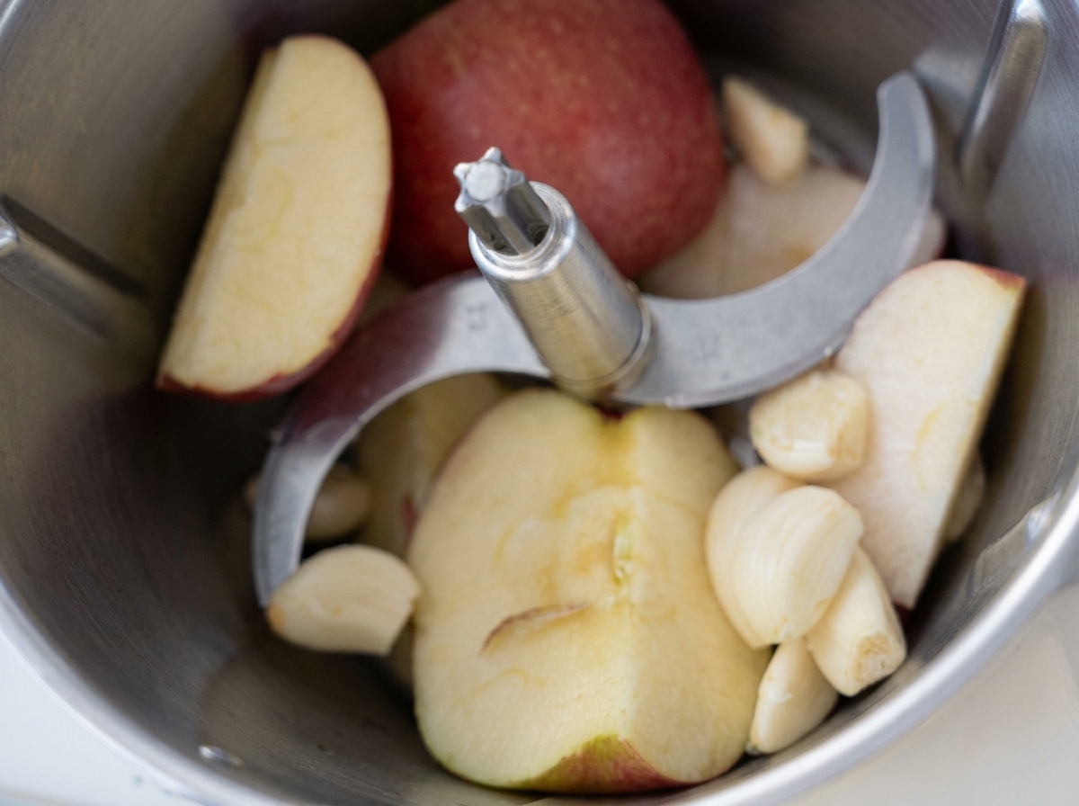 Rodajas de manzana y dientes de ajo pelados dentro del recipiente de un procesador de alimentos antes de licuar.
