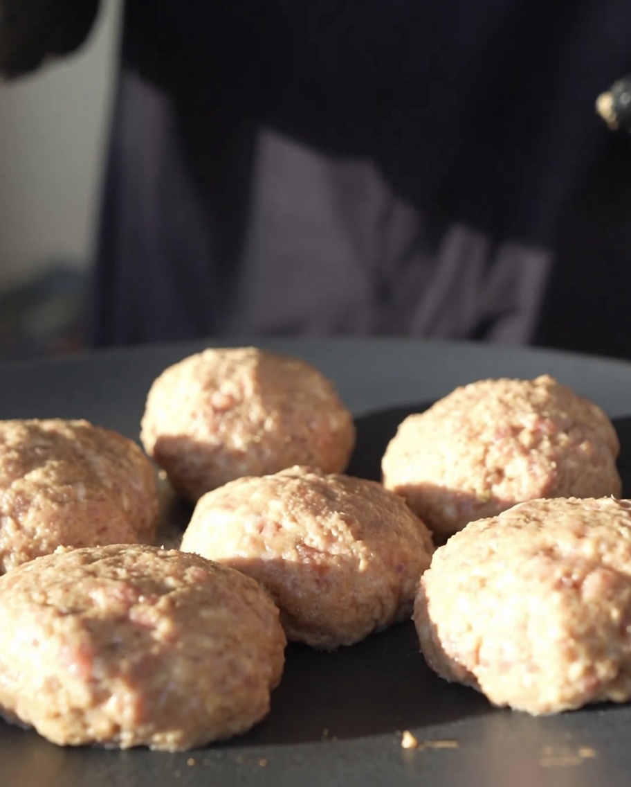 Hamburguesas de carne redondas cocinándose en una sartén de hierro fundido negra plana a fuego bajo.