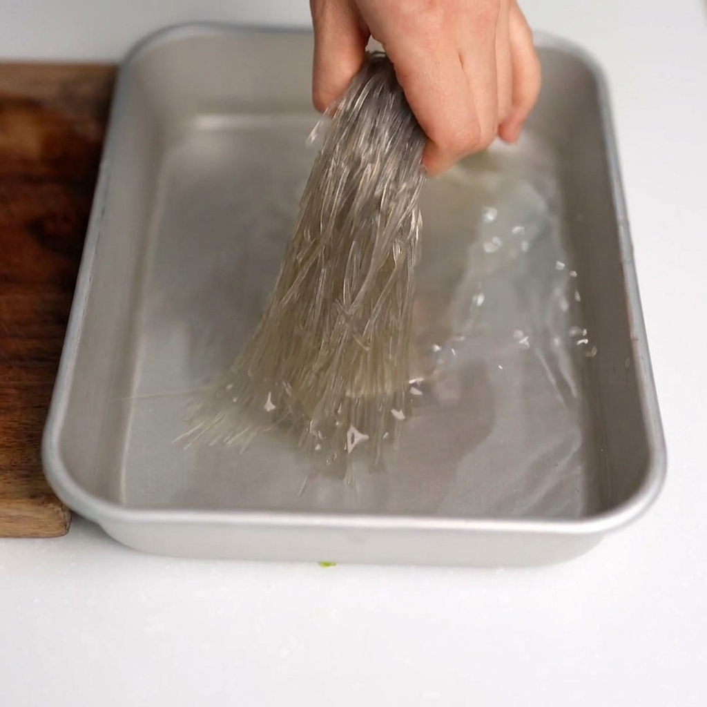Tijeras de cocina cortando fideos de cristal remojados en pequeños segmentos dentro de un bol.