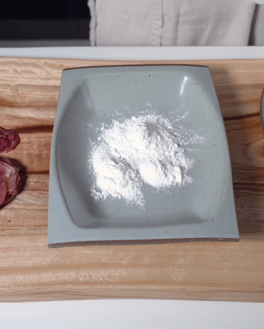 Un plato rectangular gris lleno de harina de arroz glutinoso junto a las láminas de ternera sazonadas.