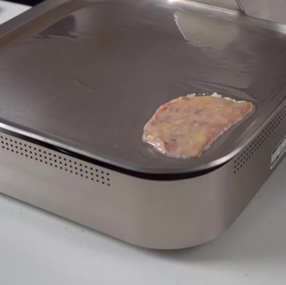 Una lámina de ternera rebozada en huevo cocinándose suavemente sobre una plancha eléctrica.