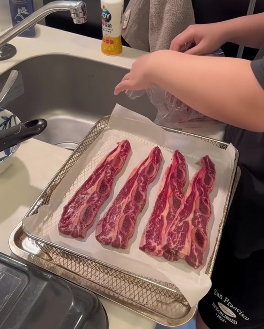Primer plano de unas manos usando toallas de papel para presionar sobre las costillas de res crudas y absorber la humedad superficial.