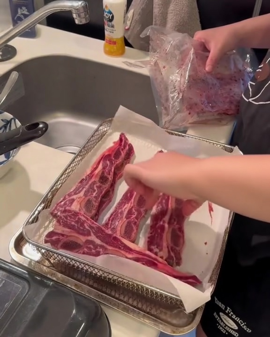 Costillas de res crudas colocadas dentro de la canasta de una freidora de aire, listas para el proceso de cocción.