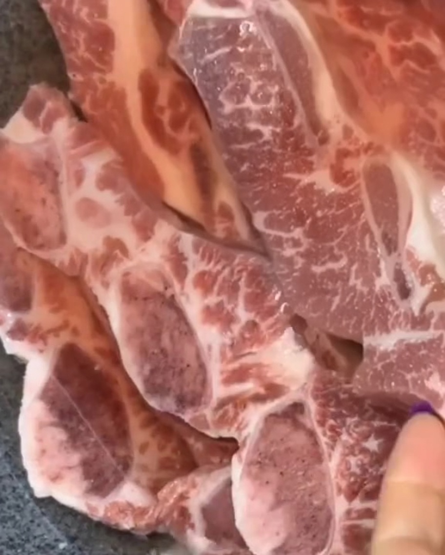 Costillas de res crudas dispuestas en un tazón oscuro.