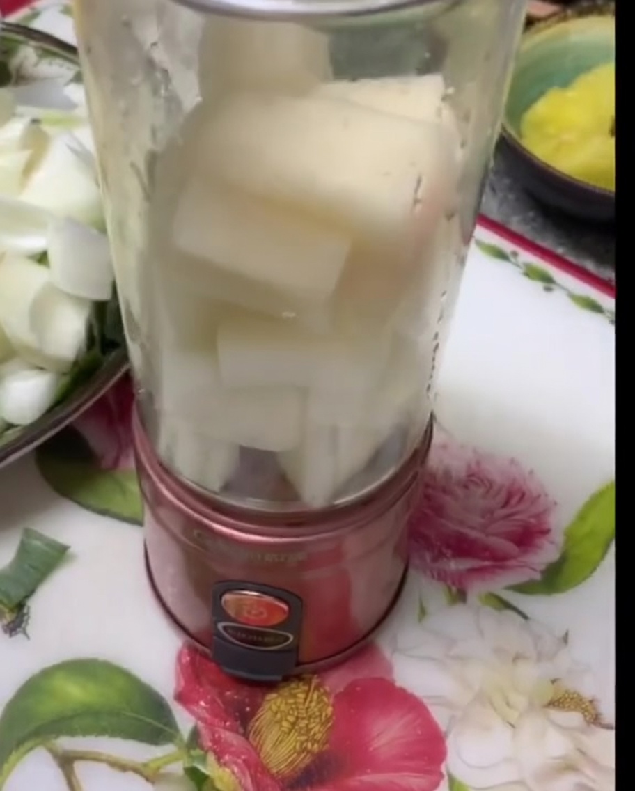 Trozos de pera blanca y cebolla apilados dentro de un vaso de licuadora transparente.