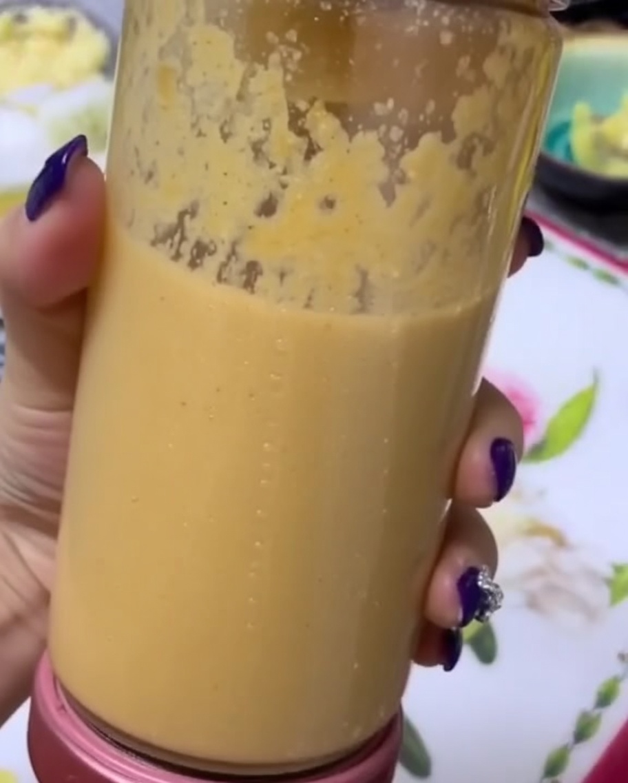 Una mano sosteniendo un vaso de licuadora lleno de un puré de frutas y verduras suave y espeso.