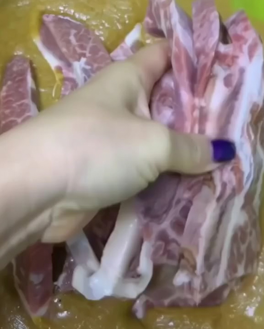 Una mano sumergiendo trozos de costillas de res crudas en un marinado espeso en un tazón verde.