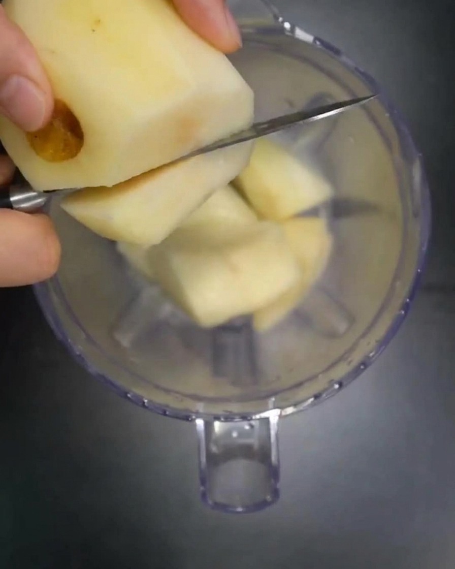 Trozos de pera, manzana y cebolla fresca siendo añadidos al vaso de una licuadora.