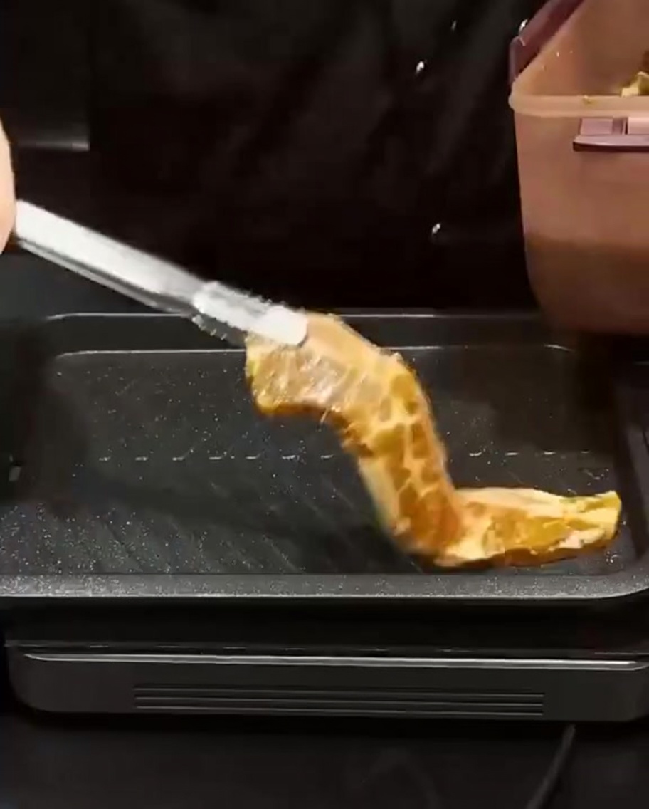 Costillas marinadas siendo colocadas con pinzas sobre una parrilla rectangular caliente para sellarlas.