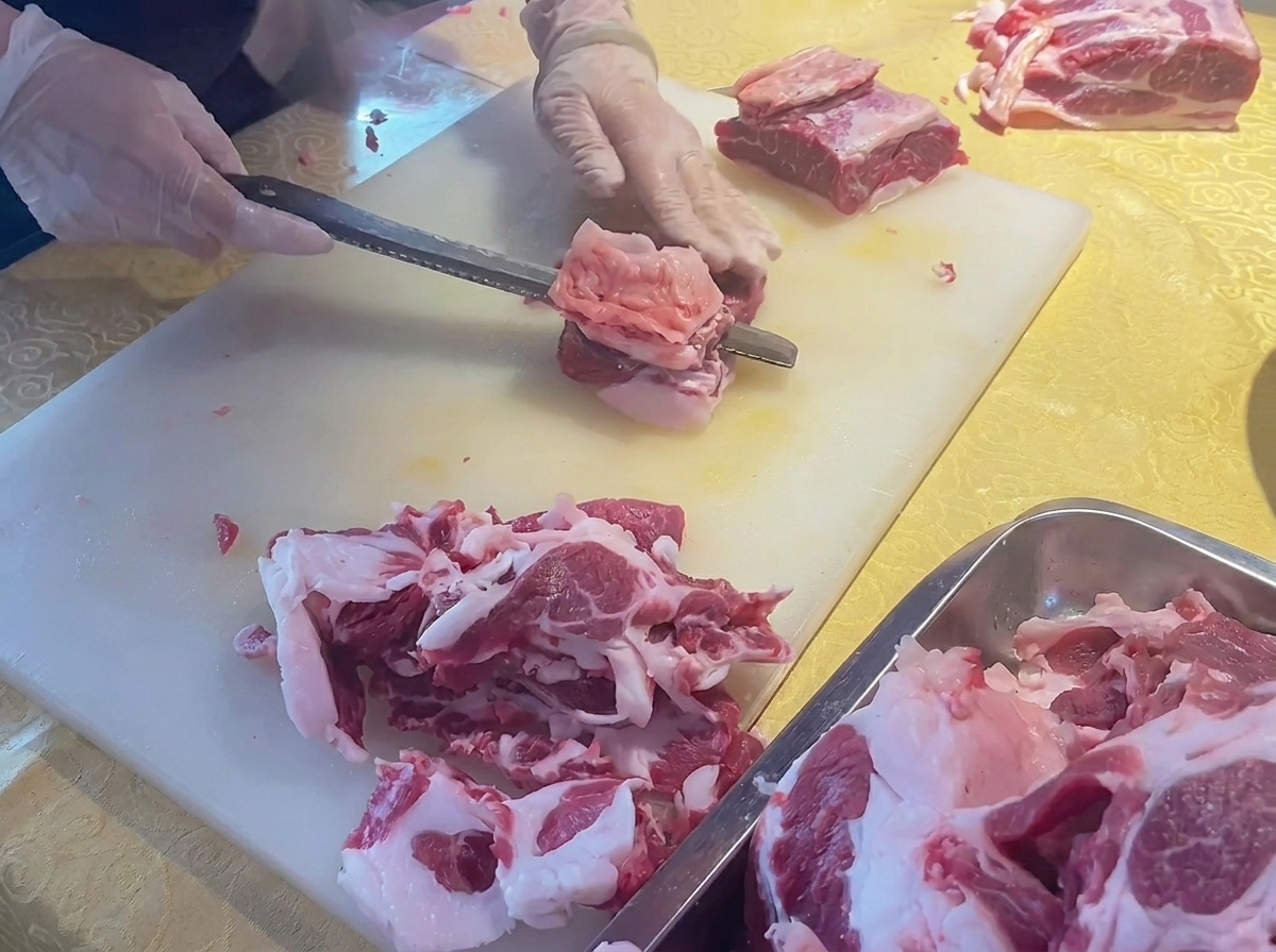 Manos usando un cuchillo para recortar el exceso de grasa de un corte de costilla de ternera fresca sobre una tabla de cortar blanca.