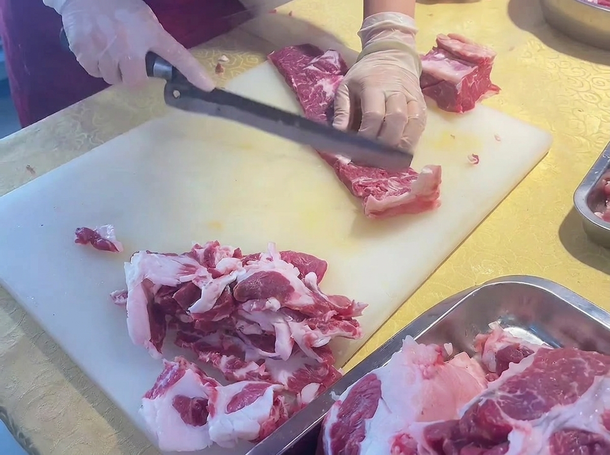 Manos cortando una costilla de ternera recortada en piezas finas usando un cuchillo largo en ángulo.