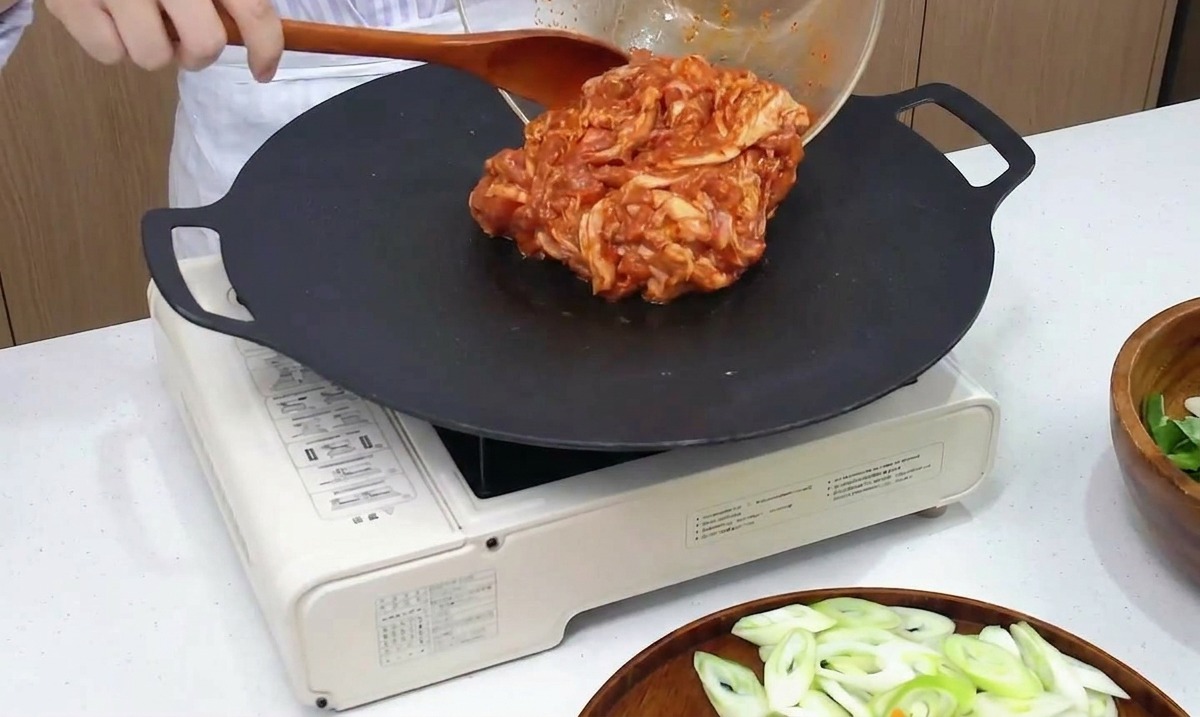 Panceta de cerdo picante marinada vertiéndose desde un bol de cristal sobre una plancha negra caliente.