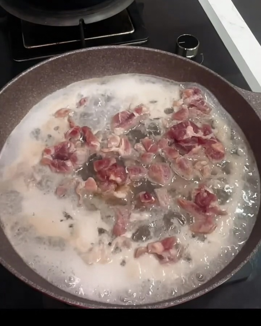 Trozos de cerdo hirviendo en una sartén con agua, vino de cocina y una hoja de laurel.
