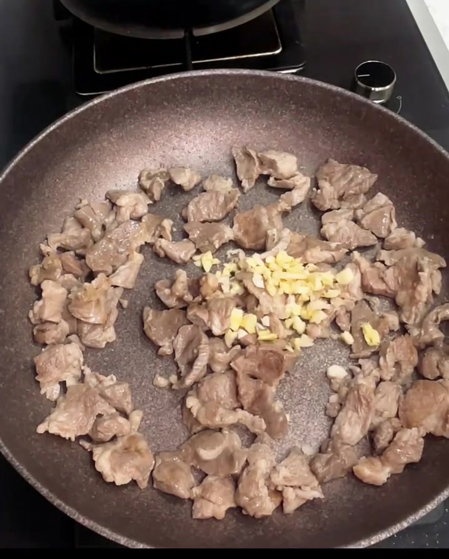 Trozos de cerdo salteándose en una sartén con ajo recién picado añadido.