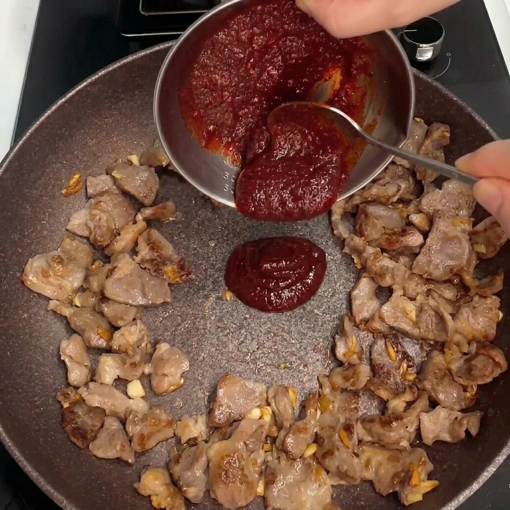 Salsa roja espesa vertida en el centro de la sartén con el cerdo salteándose.