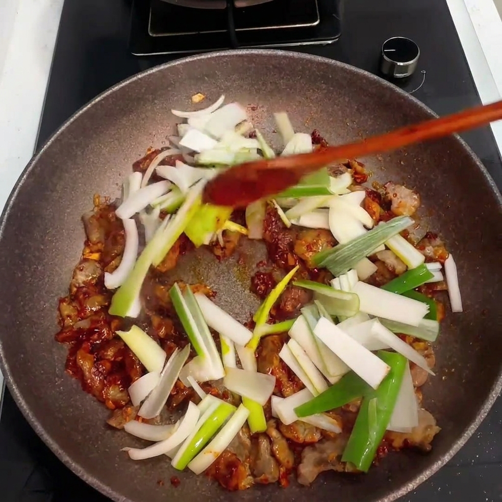Cebollas y tallos de cebolleta recién picados añadidos a la sartén con el cerdo y la salsa.