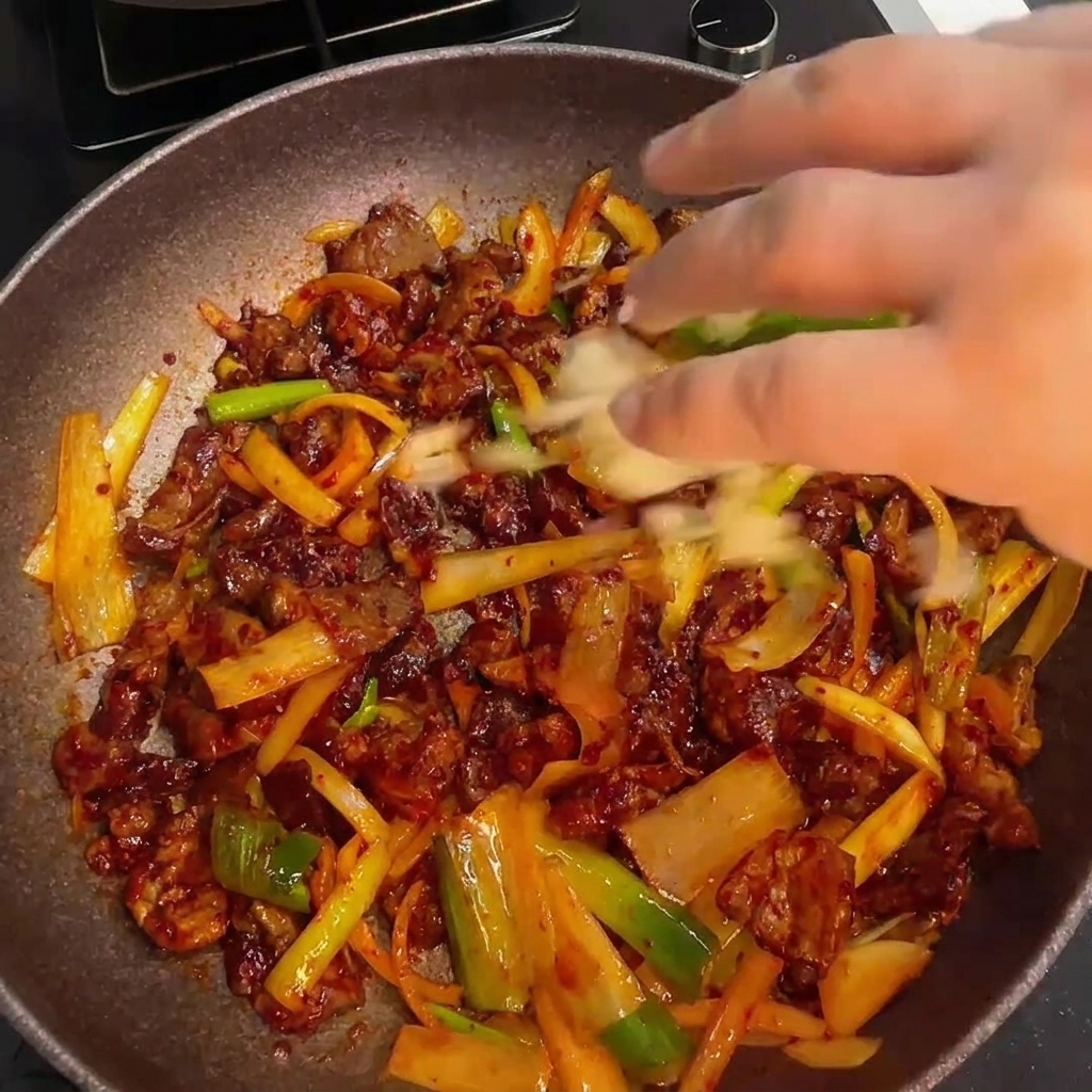 Finalizando el salteado de cerdo picante mezclando ajo fresco y un chorrito de aceite de sésamo.