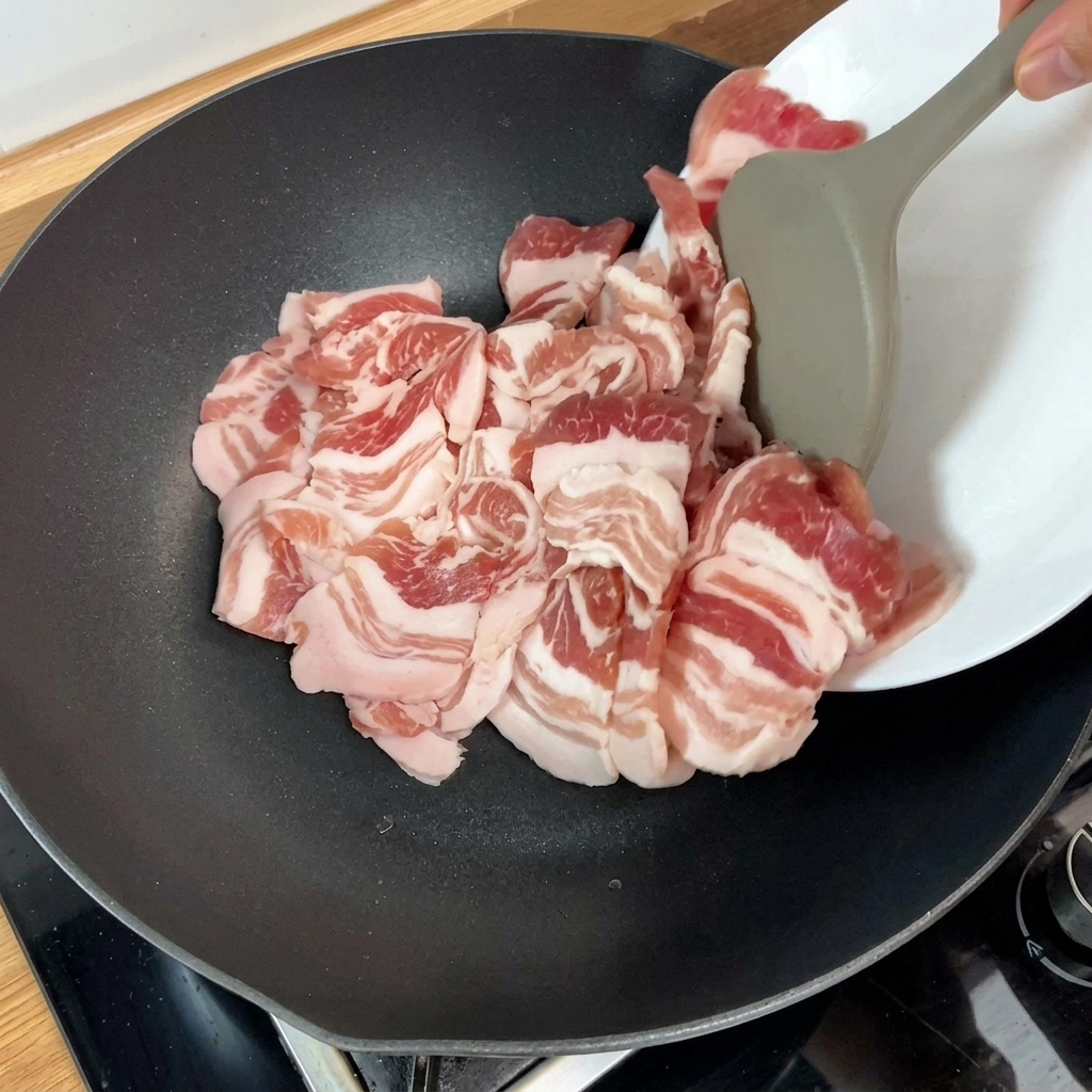Lonchas de panceta cruda siendo añadidas a una sartén caliente con una herramienta de cocina.