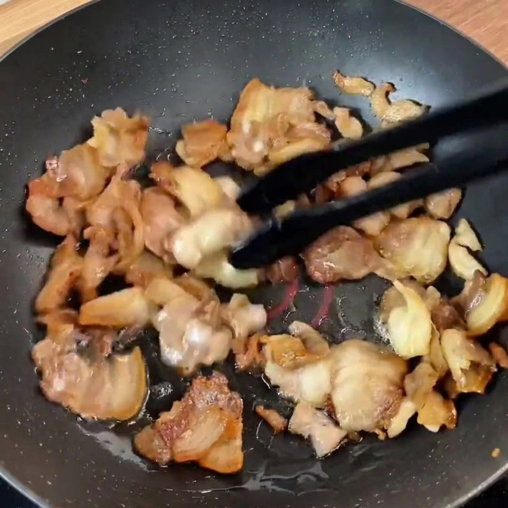 Tiras de pimiento verde y cebolla morada sobre la carne sellada en la sartén.