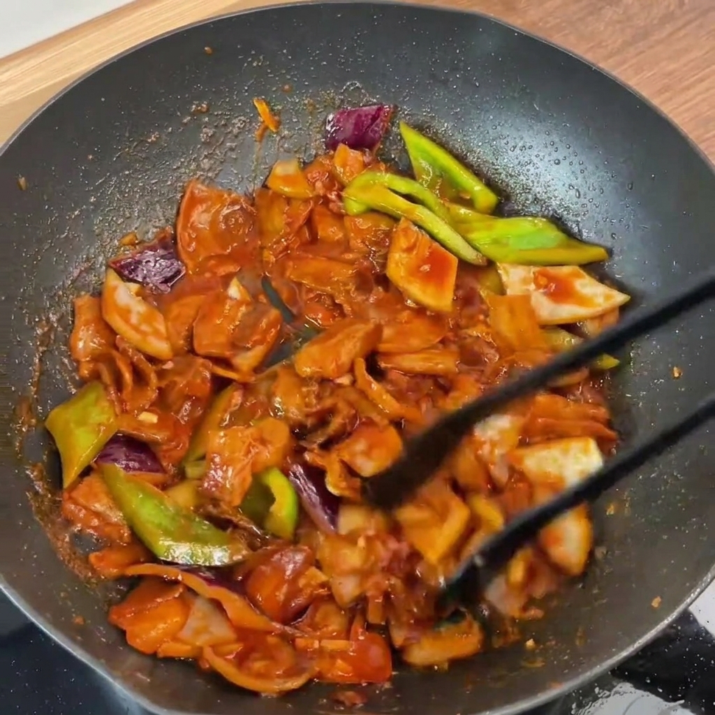 El cerdo y las verduras terminados, siendo mezclados en la sartén y cubiertos con la salsa brillante.