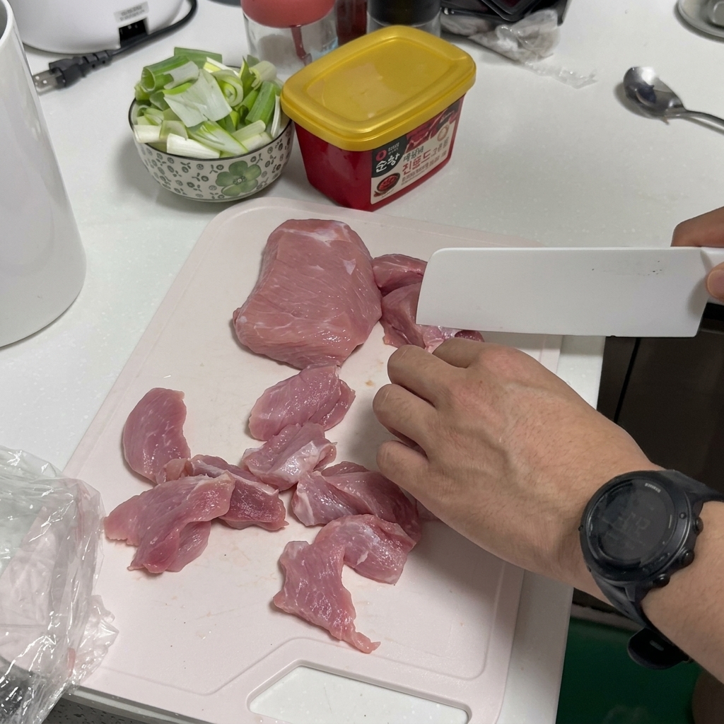 Una persona cortando cerdo crudo sobre una tabla de cortar de plástico blanca con un cuchillo de cocina blanco.