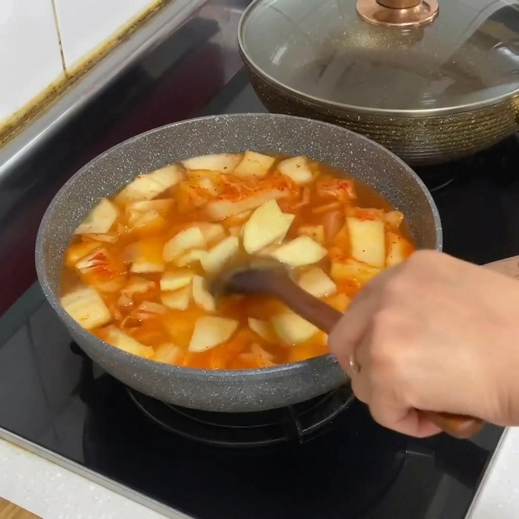 Fideos de cristal siendo añadidos a la olla de estofado de kimchi burbujeante.