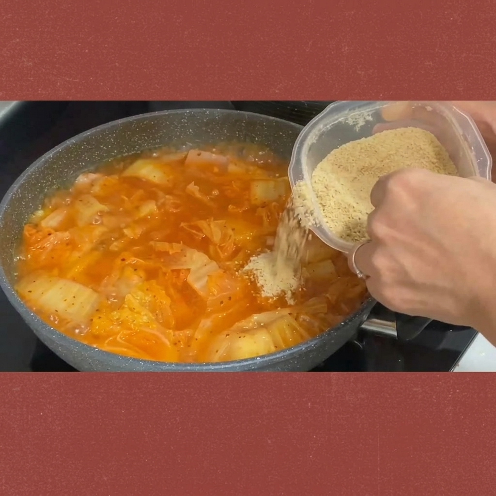 Azúcar siendo espolvoreada desde un recipiente al estofado de kimchi burbujeante.