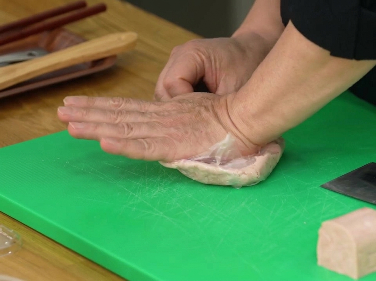 Una mano presionando una bolsa de plástico que contiene media pieza de Spam para triturarla hasta formar una pasta.