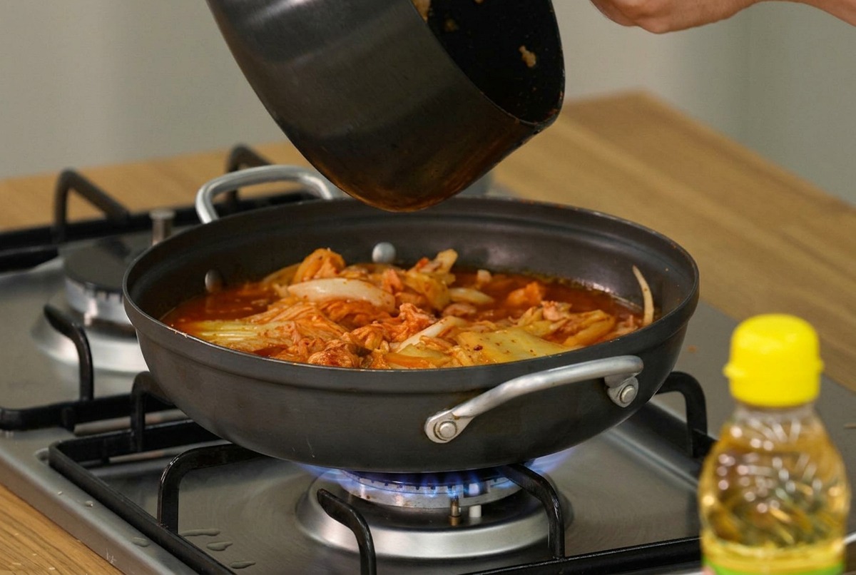 Rodajas de tofu suave y cebolletas frescas siendo colocadas con cuidado sobre la superficie del estofado de kimchi hirviendo.