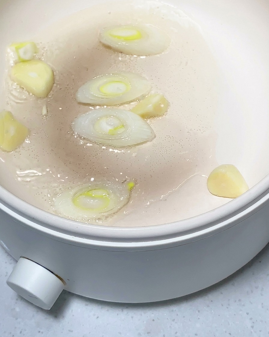 Trozos de patata, ajo picado y jengibre siendo salteados en una sartén ligeramente aceitada.