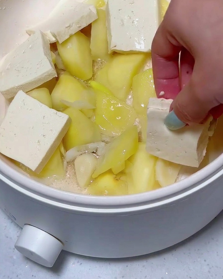 Rodajas de tofu y carne en conserva dispuestas sobre trozos de patata en la sartén.