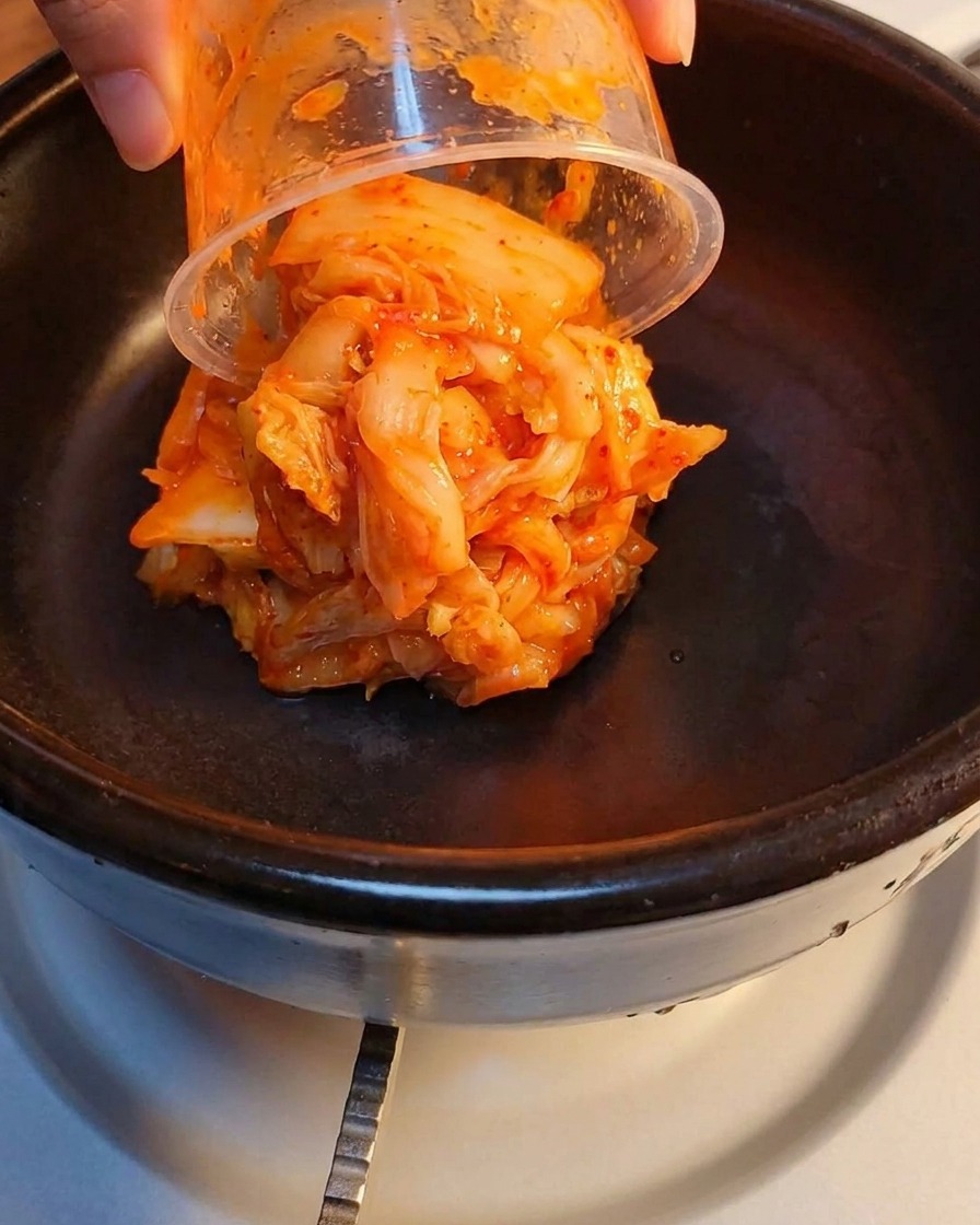 Kimchi fermentado y carne enlatada triturada en capas dentro de una olla de piedra.