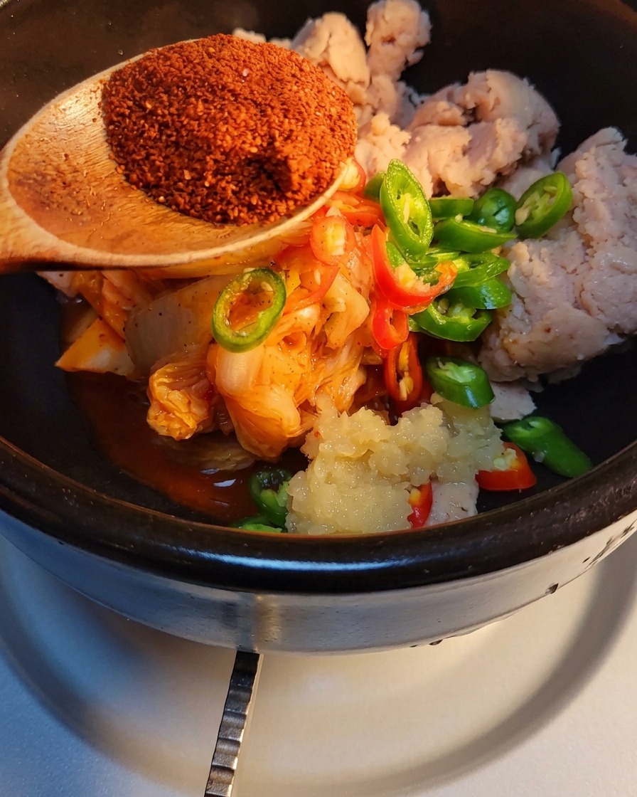 Chile en polvo coreano siendo espolvoreado sobre los demás ingredientes en la olla de piedra.