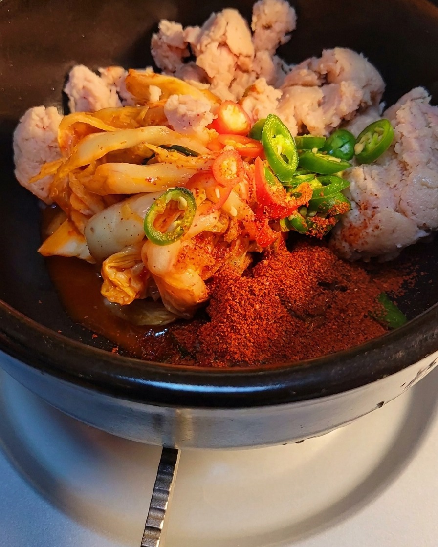 Primer plano de azúcar y sazonador de carne en polvo siendo espolvoreados sobre el kimchi y la carne enlatada en la olla de piedra.