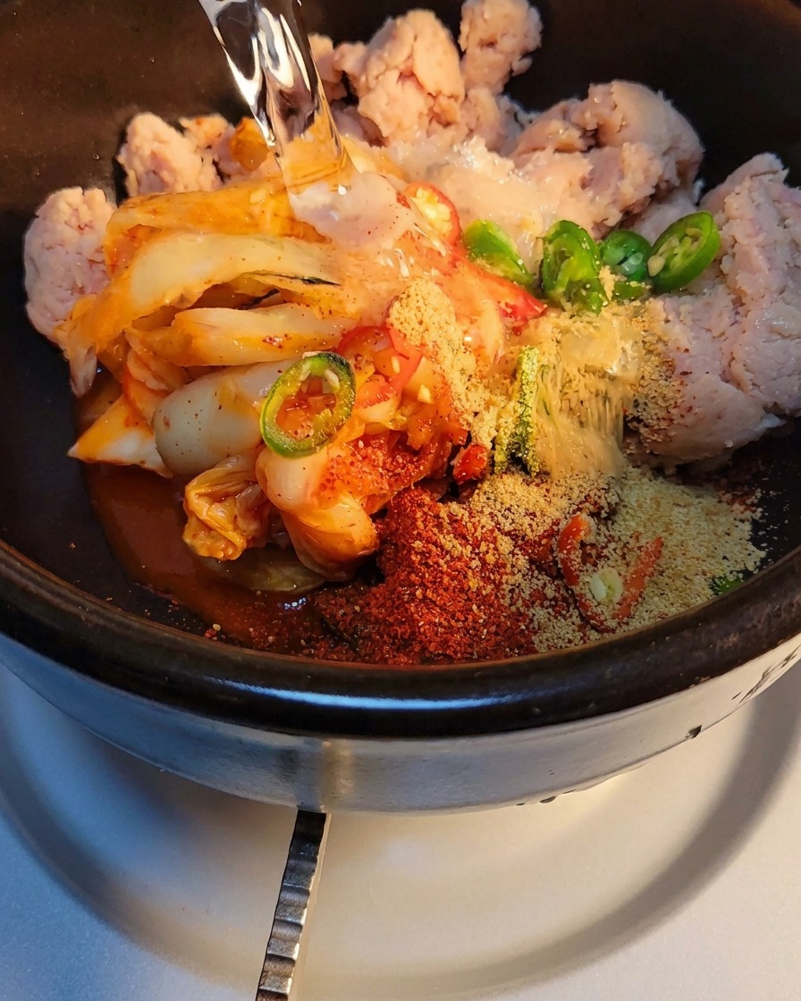 Agua siendo vertida en la olla de piedra con el kimchi y las especias, lista para ser calentada en la estufa.