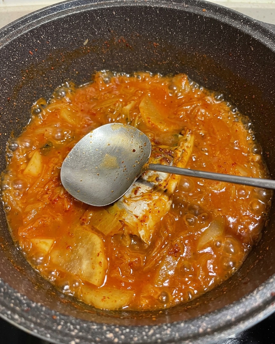 Un vibrante estofado rojo burbujeante de caballa y verduras en una olla, con una cuchara de metal levantando un trozo de pescado.
