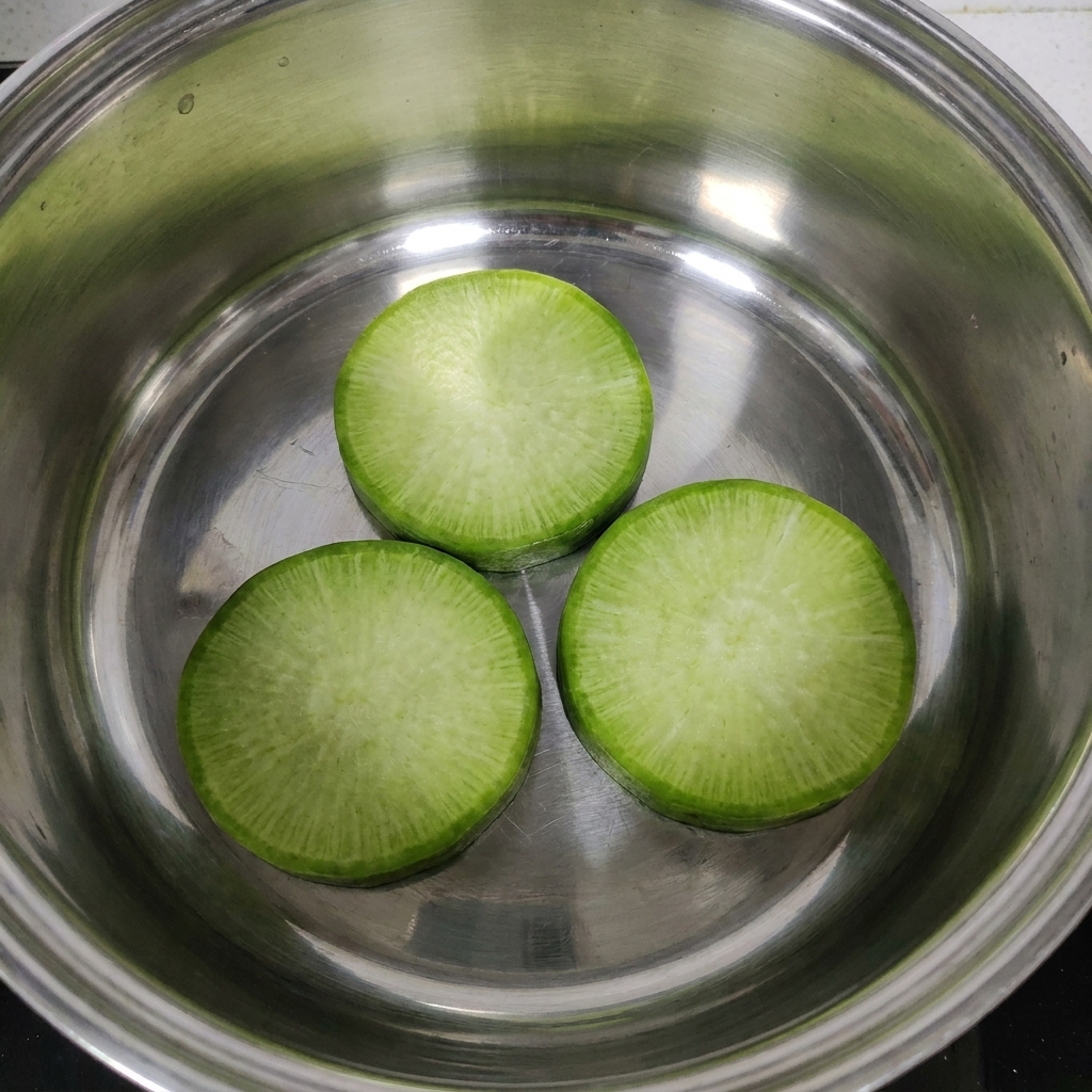 Tres rodajas gruesas de rábano colocadas cuidadosamente en el fondo de una olla de acero inoxidable.