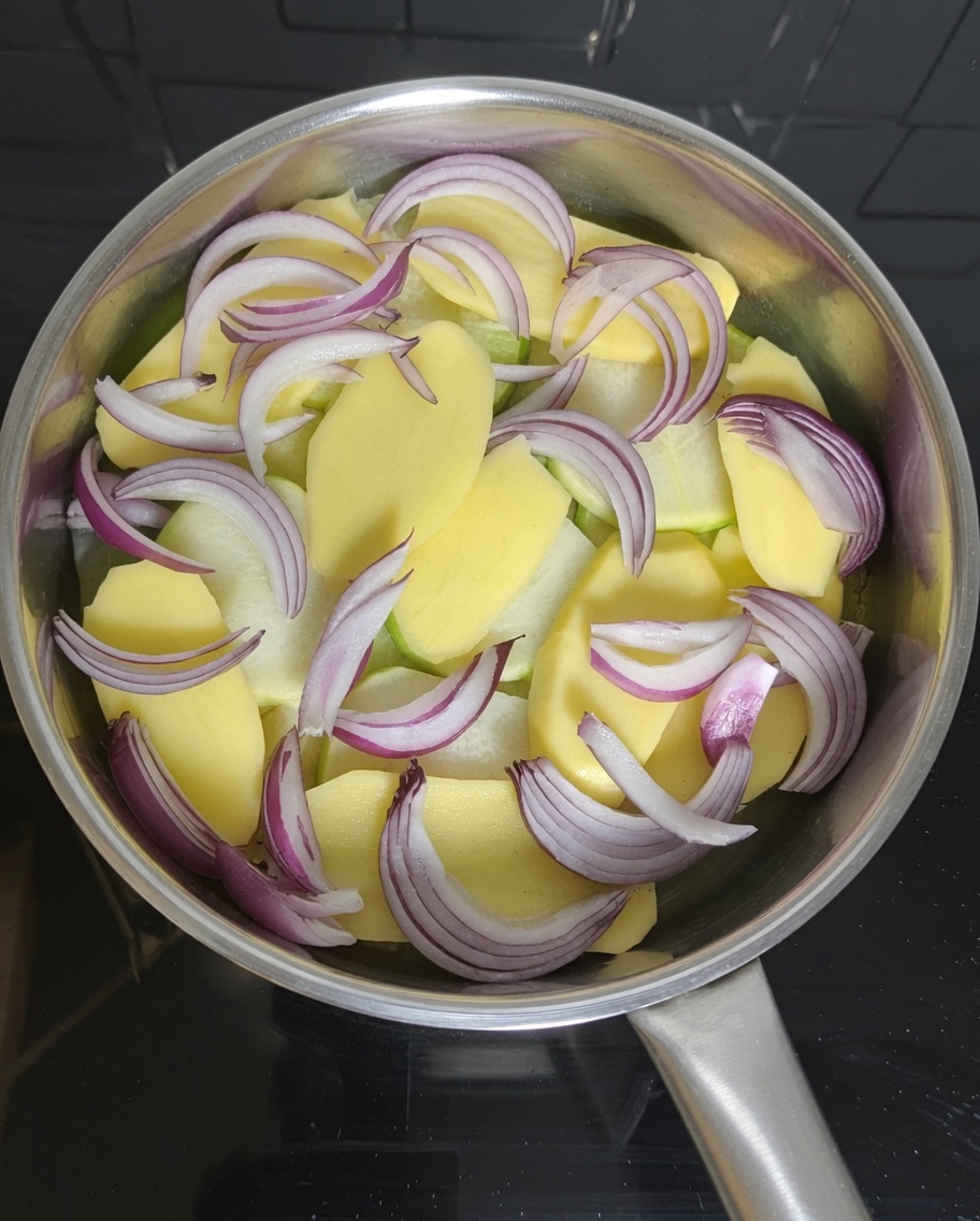 Trozos de caballa en conserva siendo dispuestos sobre rodajas de patata y cebolla en una olla.