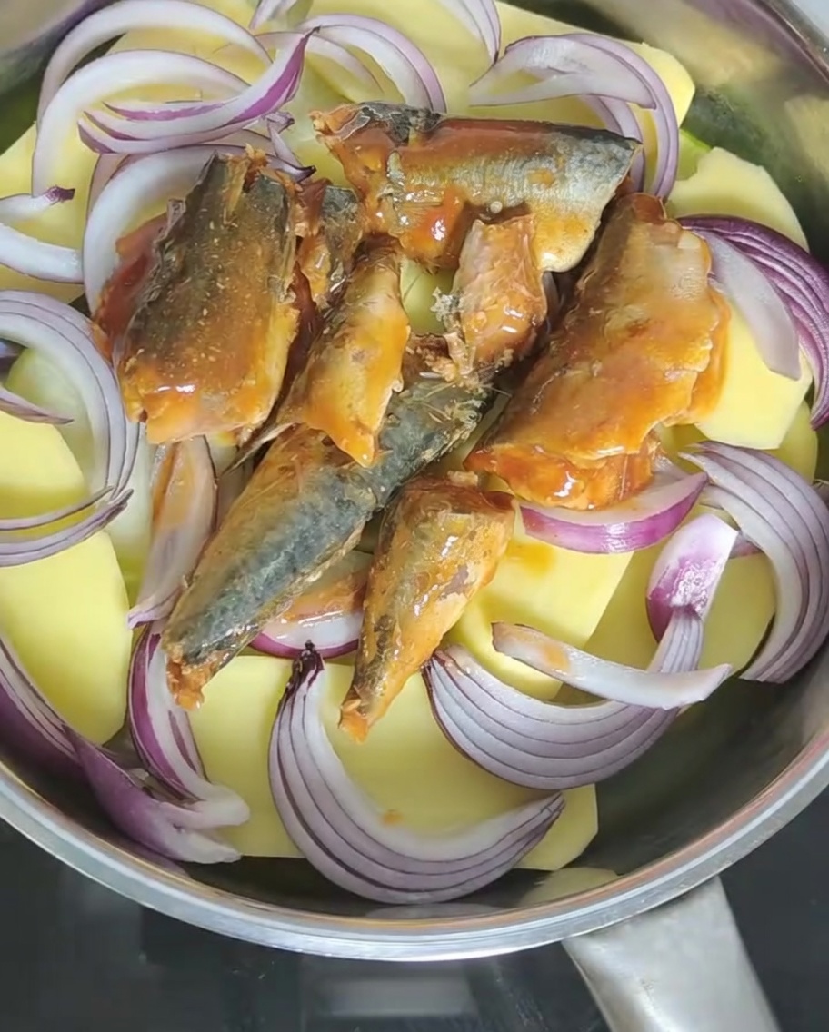 Salsa de tomate de la lata de caballa siendo vertida en la olla con otros ingredientes.
