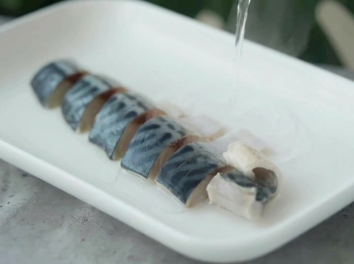 Agua caliente siendo vertida de una tetera sobre trozos de caballa dispuestos en un plato blanco.
