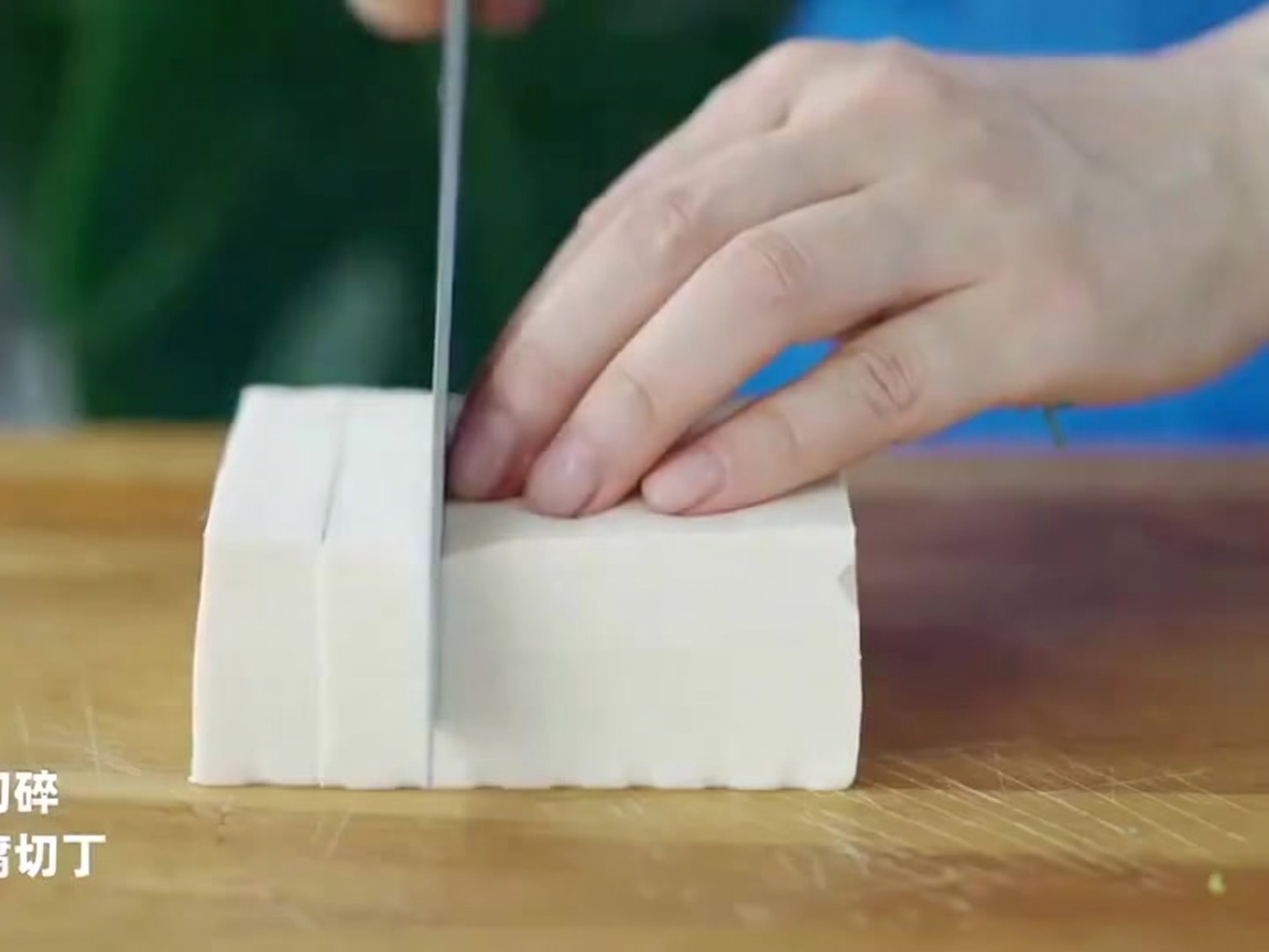 Un cuchillo de chef cortando un bloque de tofu blanco en cubos precisos y uniformes sobre una superficie de madera.