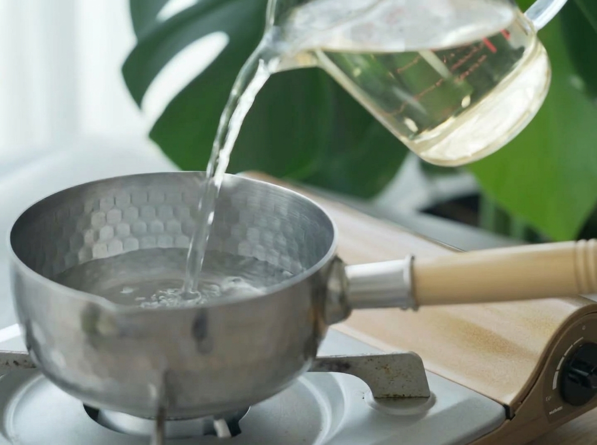 Caldo dashi transparente siendo vertido desde una taza medidora en una pequeña olla de acero inoxidable.