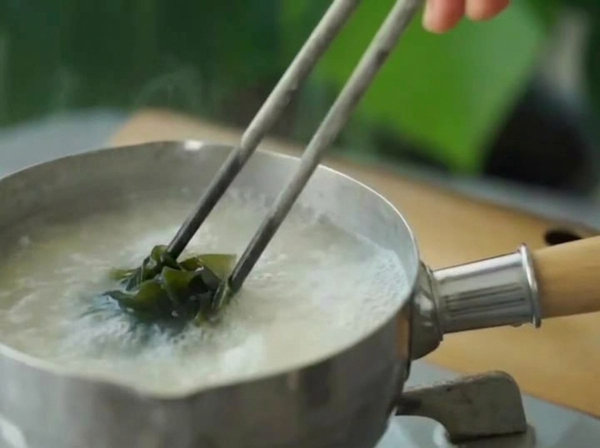 Wakame verde rehidratado siendo añadido a la sopa de miso a fuego lento usando palillos.