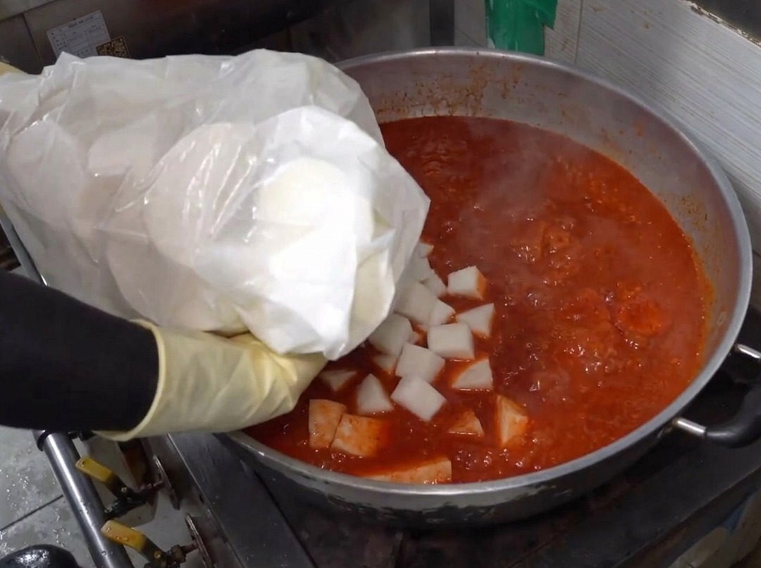 Trozos de rábano siendo añadidos a una olla grande llena de líquido rojo picante hirviendo.