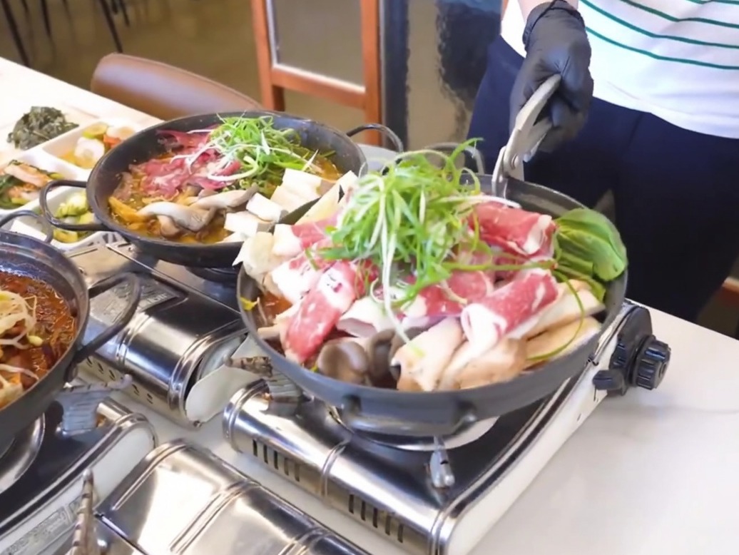 Una olla de hierro negro siendo preparada con una capa de rábano cocido y kimchi en el fondo.