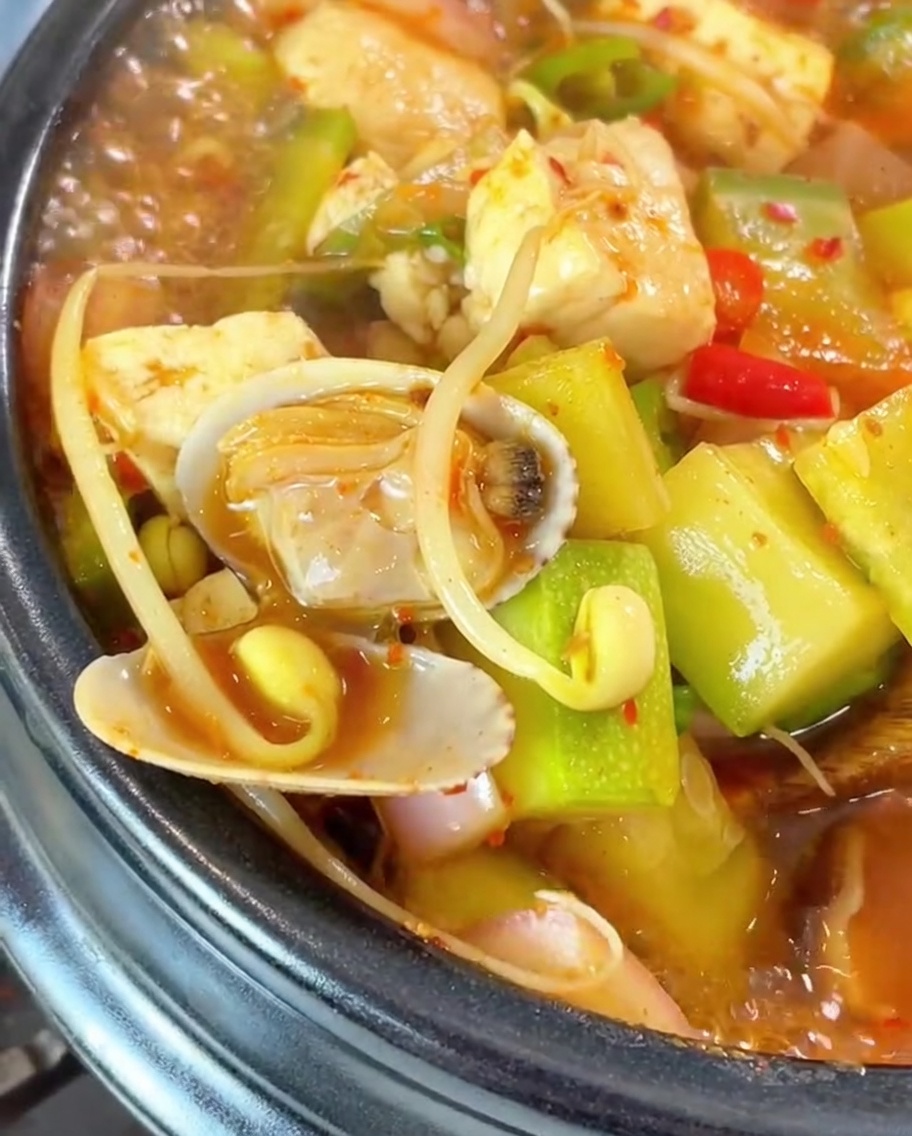 Una olla de cerámica negra sobre la estufa llena de agua de arroz y pasta de soja, siendo removida con una cuchara de madera.