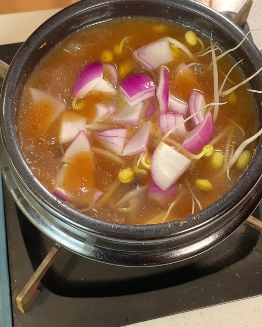 Brotes de soja, láminas de cebolla roja y tofu en cubos hirviendo en el caldo.